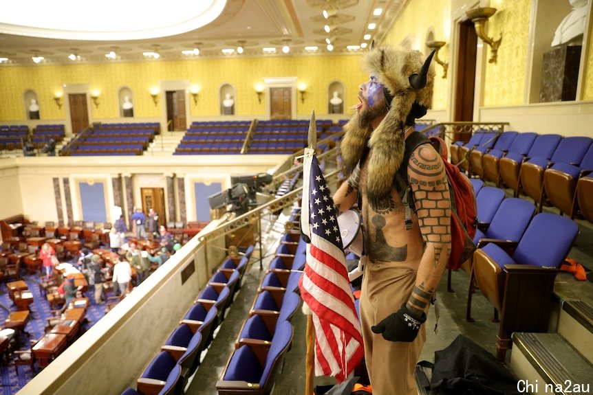 A shirtless, tattooed protester wearing a horned helmet shouts from the upstairs gallery of the US Senate.