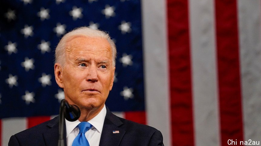 Joe Biden glances to his left in front of a large American flag