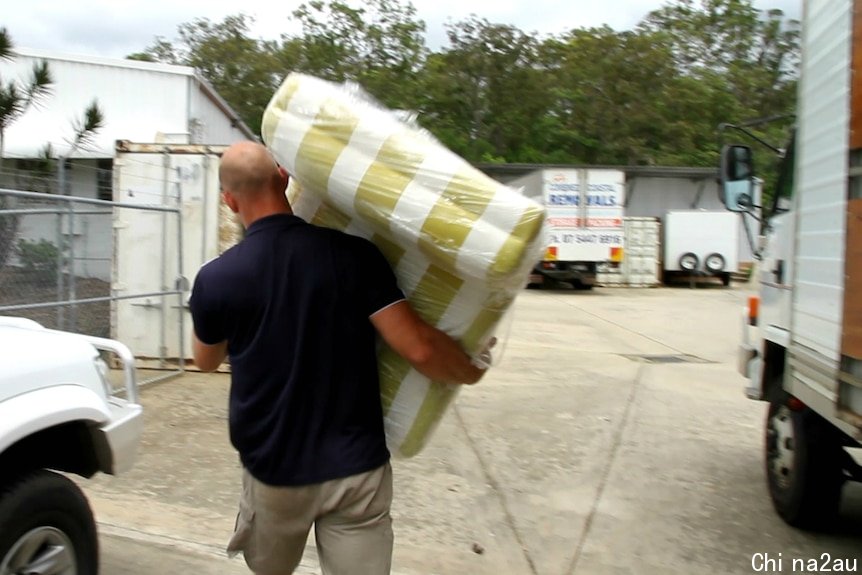 A man walking away carrying a striped lounge chair wrapped in plastic.