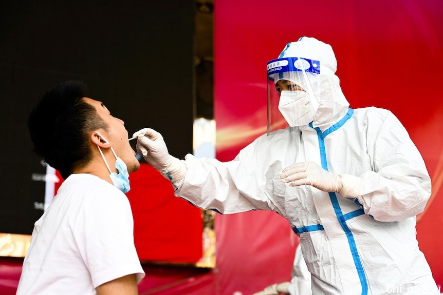 一个穿着全套防护装备的护士把棉签插进一个男人的喉咙里。