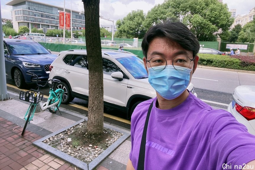 穿着紫色T恤戴着蓝色口罩的年轻中国男子。