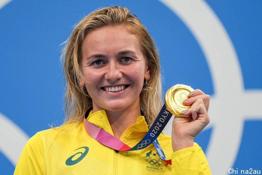 Ariarne Titmus holds up her gold medal at the Tokyo Aquatics Centre.