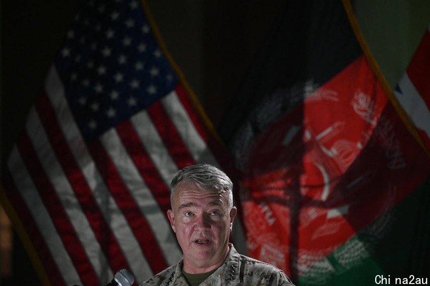 A military general in fatigues speaks in front of US and Afghan flags