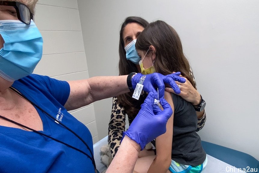 A nine-year-old girl is held by her mother as she gets the second dose of the Pfizer COVID-19 vaccine during a clinical trial.