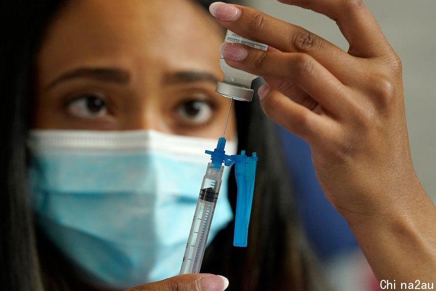 A healthcare worker wearing a face mask draws COVID-19 vaccine into a syringe