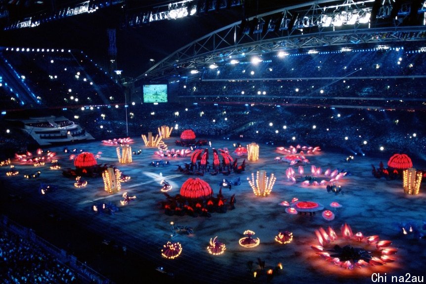 A stadium filled with people watching performers dancing around light sculptures