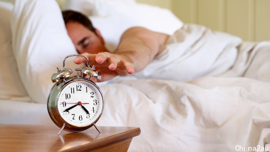 A man reaching out for an alarm clock while still in bed.