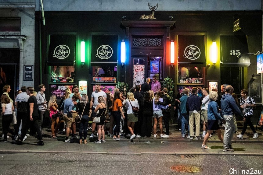 A crowd on a foodpath outside a bar with signs saying 