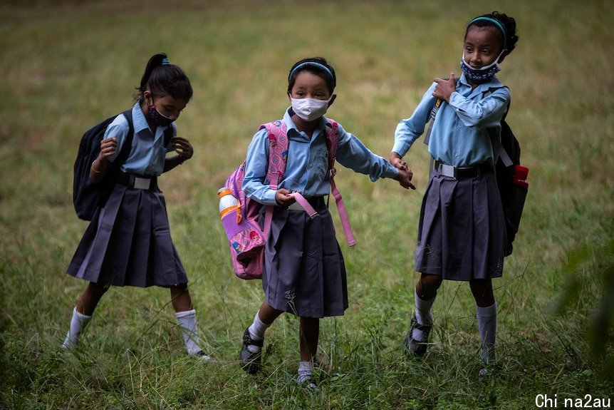 Three young girls stand in a field, wearing navy blue uniforms and face masks. 
