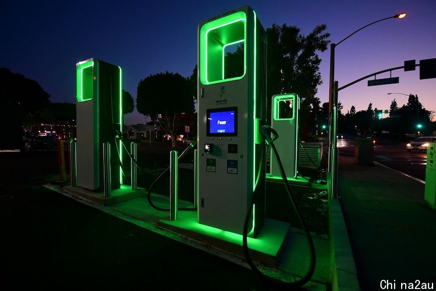 Green-glowing obelisks with charger cables by a roadside at night