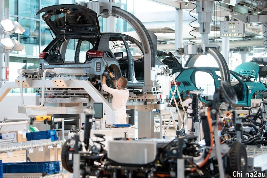 A man drills together a partially assembled car in a busy factory