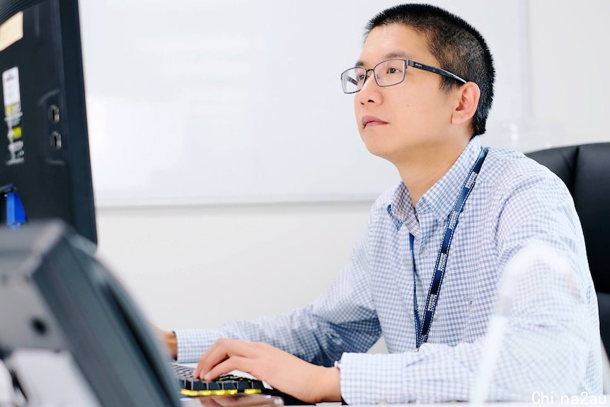 一名戴眼镜，穿衬衫的男性坐在电脑前