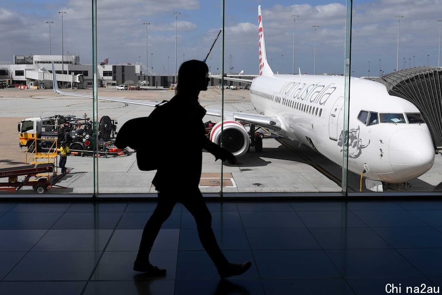 The photo shows the silhouette of a woman walking inside Melbourne Airport as a plane prepares for boarding.