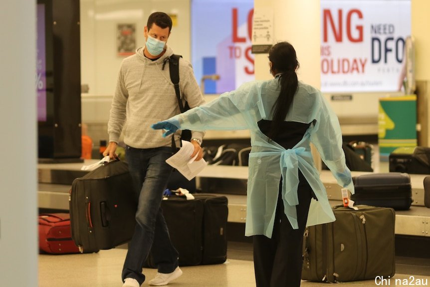 一名拿着行李的男子在机场面对一名穿着防护服的医务人员