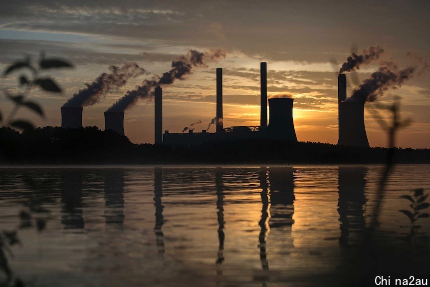 Smoke rises into the air from chimneys in front of an orange sky.