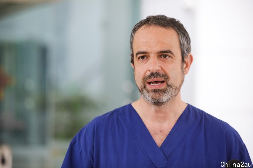 A man from mid-chest up wearing blue scrubs.