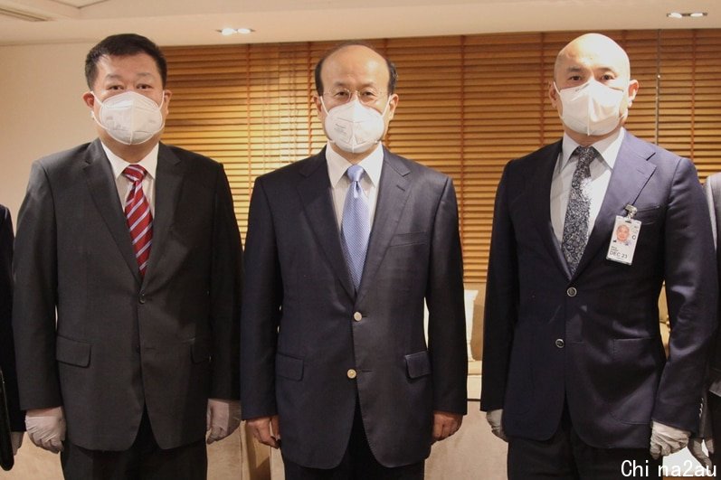 Five men wearing masks and suits pose for a photo inside an office.