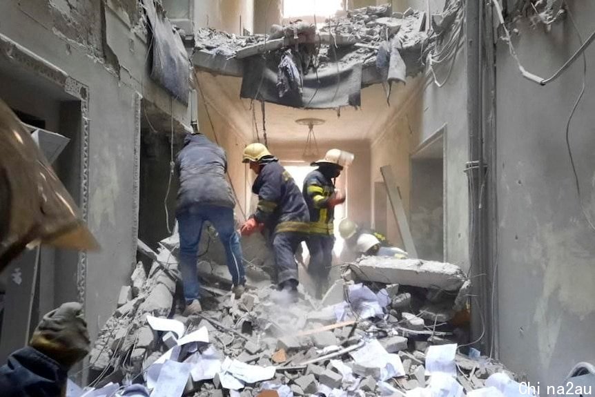 Rescue workers in helmets climb over piles of ash and debris inside a damaged building