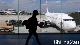 The photo shows the silhouette of a woman walking inside Melbourne Airport as a plane prepares for boarding.