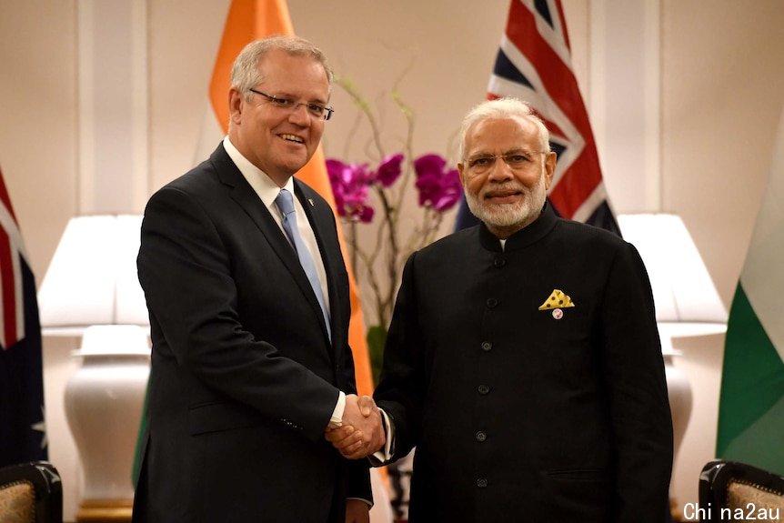 Scott Morrison, left, shakes hands with Narendra Modi, right, as they both look into the camera.