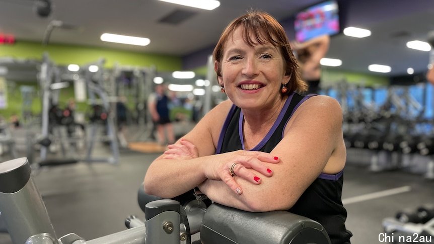 Raelene Roede is sitting on exercise equipment inside a gym and smiling at the camera