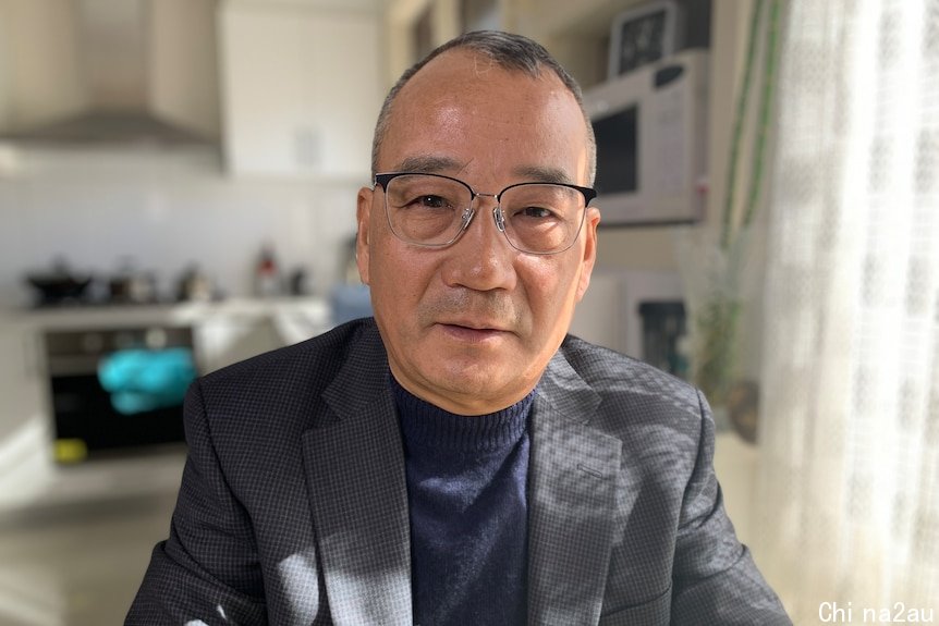 A man with glasses and grey blazer sitting in a room in a house.