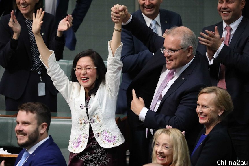 Scott Morrison holds Gladys Liu's arm in the air as he points to her with his other hand. MPs behind are smiling and clapping