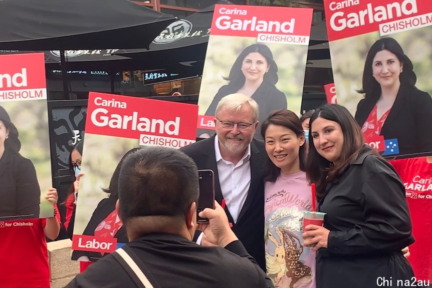 Three people pose for a photo amid red Labor campaign posters.
