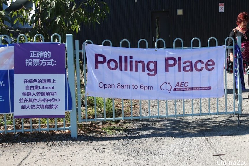 A poster in purple and white is attached to a fence next to an official AEC polling poster.