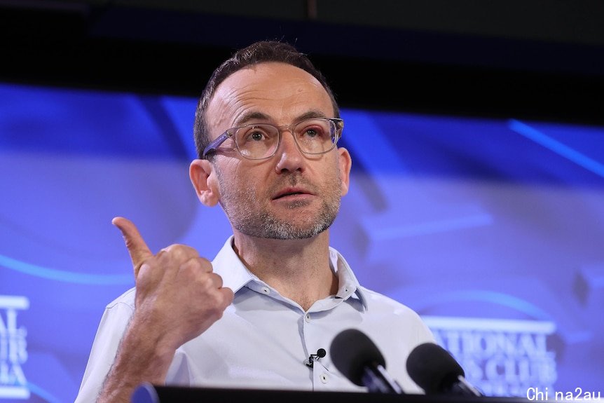 Adam Bandt stands behind a lectern with his thumb up.