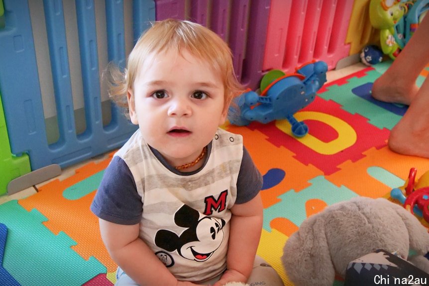 Baby boy sits on colourful floor in playpen