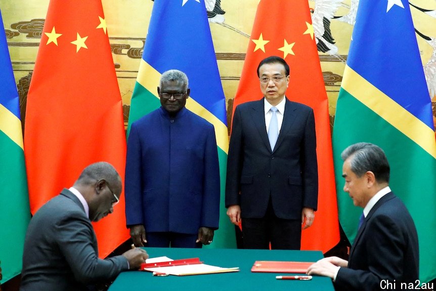 Manasseh Sogavare and Li Keqiang smile in front of Solomon Islands and Chinese flags as people sign documents.