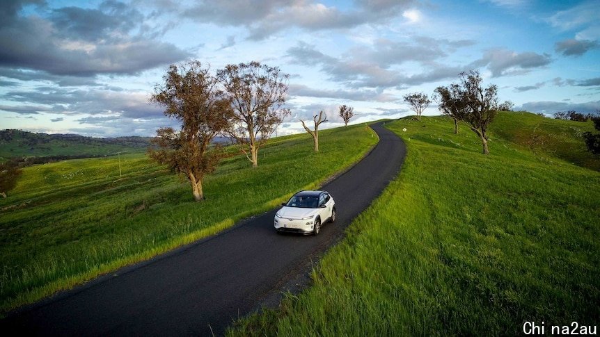 An electric car drives through green countryside.