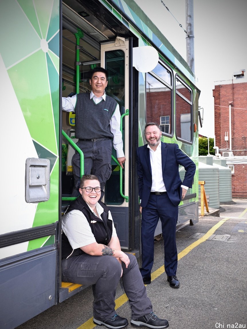 Three people smiling at the camera at an opening of a tram