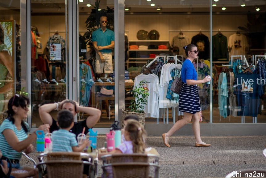 A woman walking past a group sitting at a table in the Smith St Mall, in the Darwin CBD.