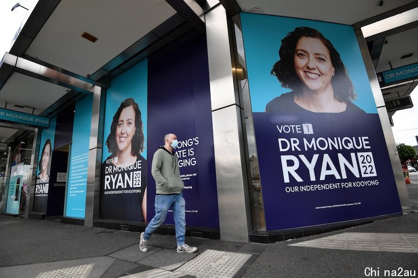 A man wearing a mask walks past large posters of Kooyong candidate Monique Ryan on a building.