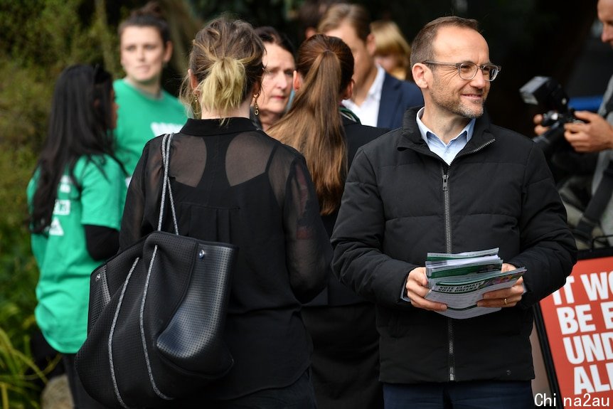 A man holding a stack of papers smiles in a crowd.