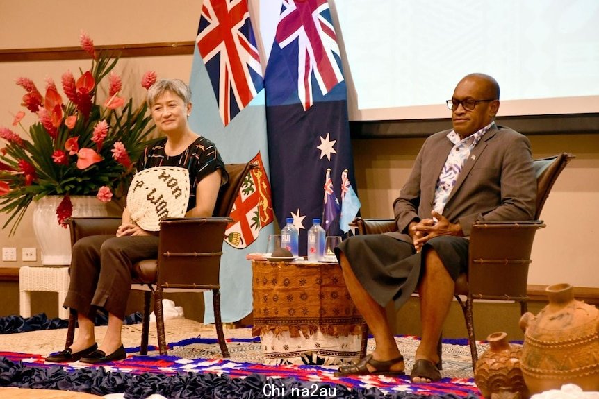 Penny Wong sits on stage behind's Fiji's Minister for Infrastructure and Meteorological Services Jone Usamate.