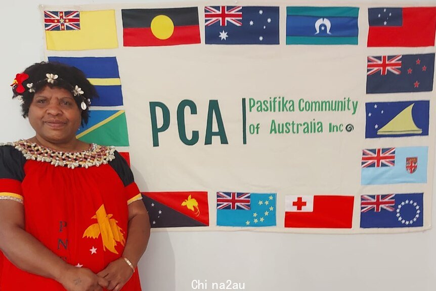 Vicki Kinai stands in front of the Pasifika Community of Australia flag. 