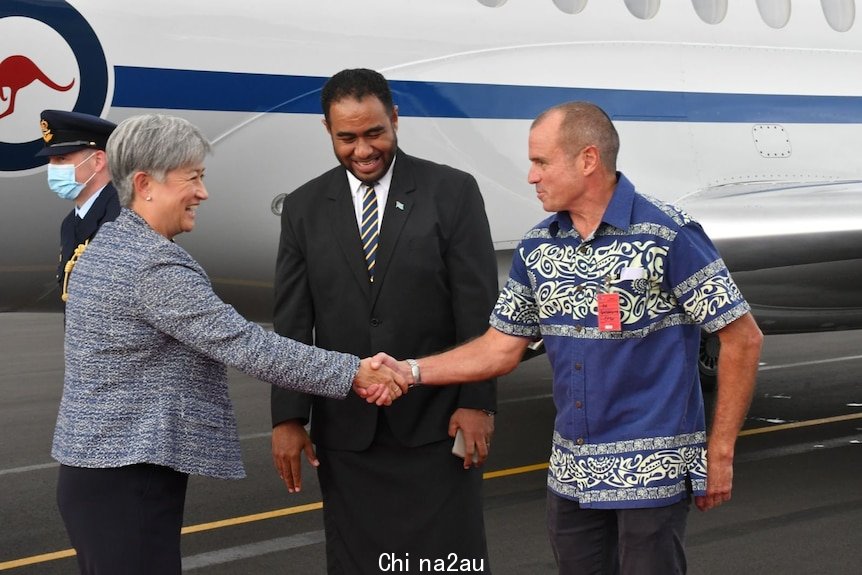 澳大利亚外交部长黄英贤穿着西装，在停机坪上和一名男子握手