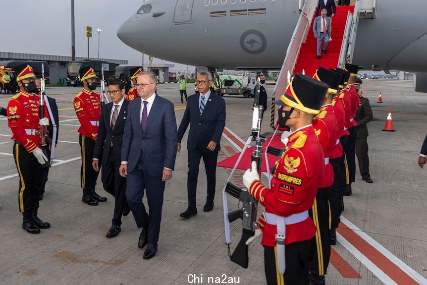 Prime Minister Anthony Albanese is flanked by soldiers in red as he walks on airport tarmac with plane behind him