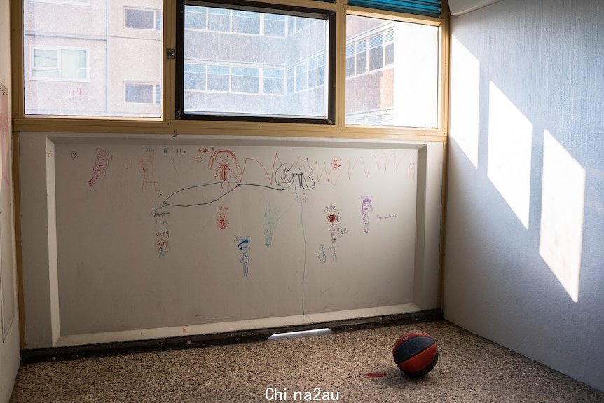 A child's drawings mark an apartment wall beneath a window. A basketball sits on the bare floor.