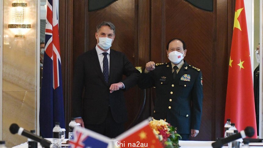 Richard Marles and Wei Fenghe bump elbows as they wear masks and stand near their countries flags
