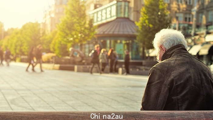 An old man sits alone on a bench in the middle of a city square