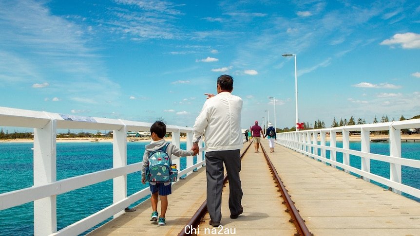 A man and a child walk along a long wooden jetty.