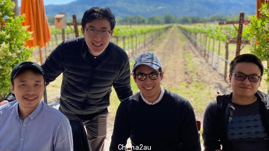 Four men sitting in front of a vineyard. 