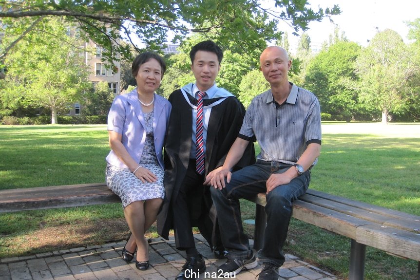 A young man in graduation robes sits with his parents