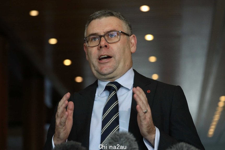 Murray Watt holding a press conference, gesticulating with his hands. He's wearing glasses.