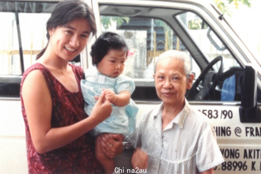 一个抱着幼儿的年轻妇女和一个老年妇女站在一起。两个女人都在微笑。