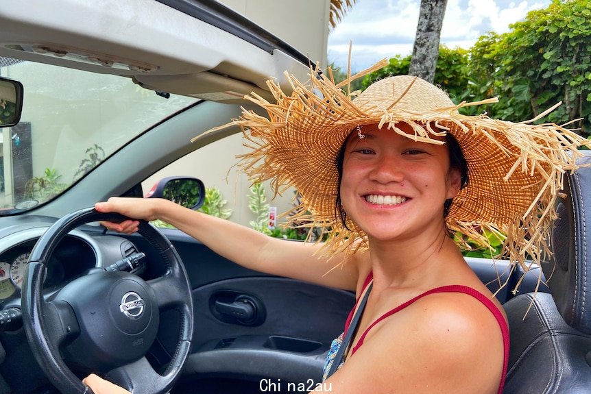 An Asian woman smiling while driving with a beige hat 